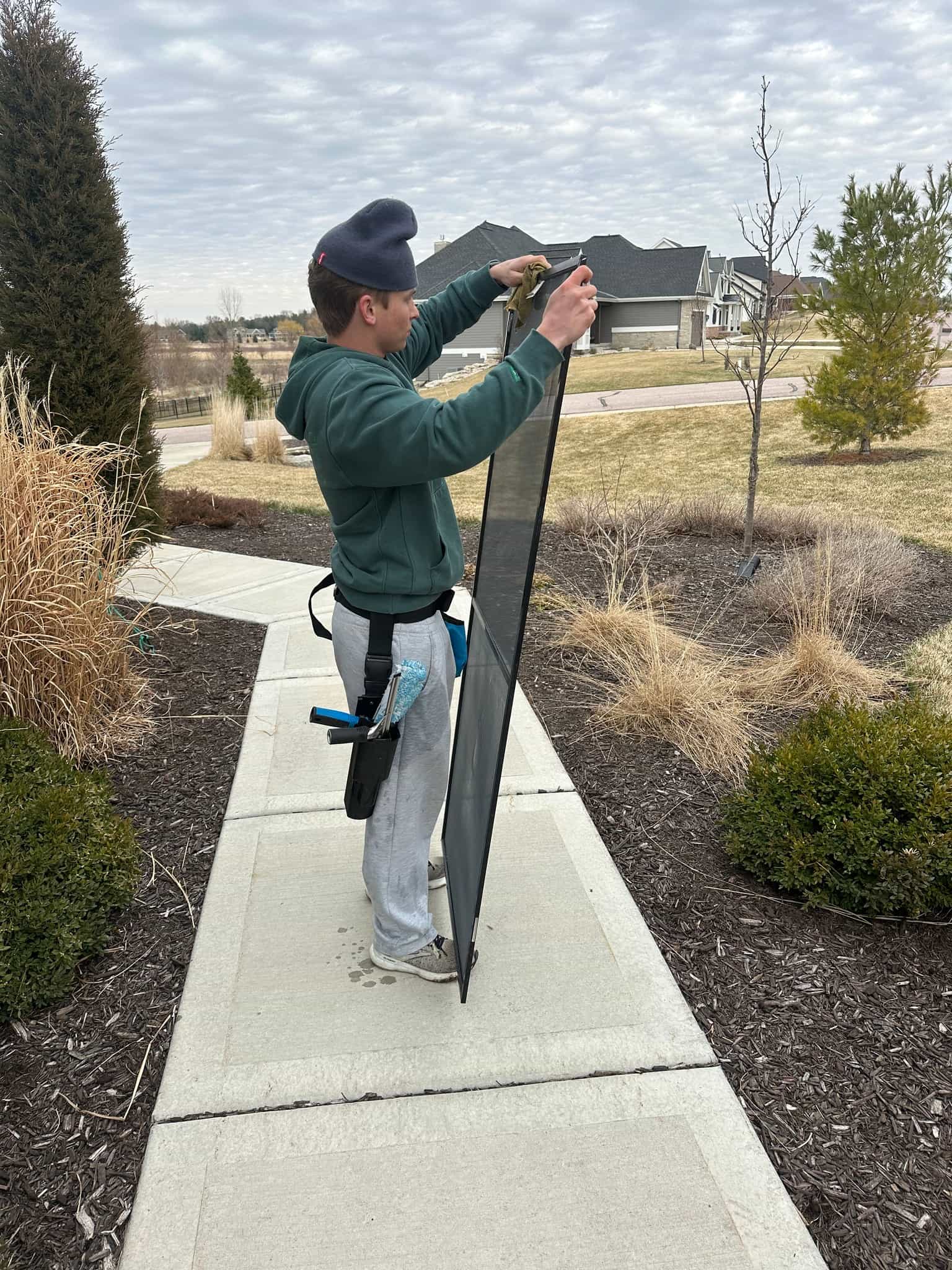 Tony Genco of Pure View Window Cleaning wiping down a window screen outside a Sun Prairie, WI home